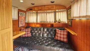 A cozy RV interior with a tufted leather sofa, wooden cabinets, and a window with curtains.