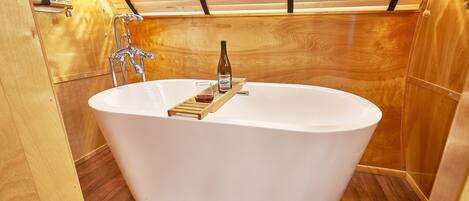 Un baño moderno con una bañera independiente, suelo de madera y techo de madera con listones.