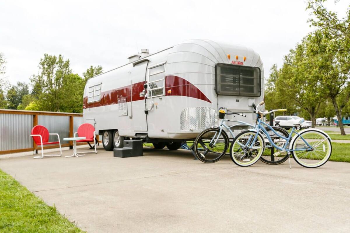 A recreational vehicle (RV) parked on a concrete surface with a bicycle and a small table with chairs nearby.