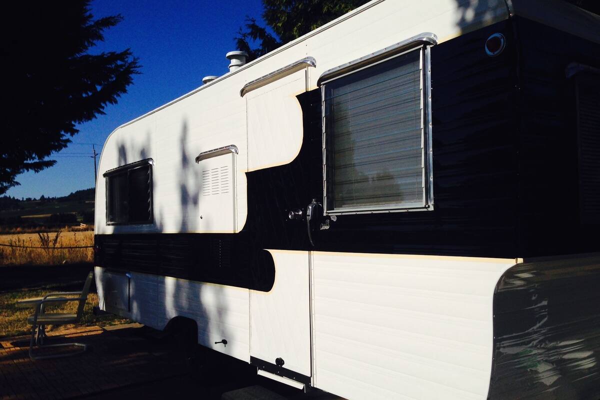 A white RV with a sliding door and a window, parked outdoors with trees and a clear sky in the background.