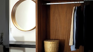 A wooden wardrobe with a circular mirror, a hanging rod with clothes, and a wicker basket. - Hotel Ix by San Clemente Business Class (Tlaxcala)