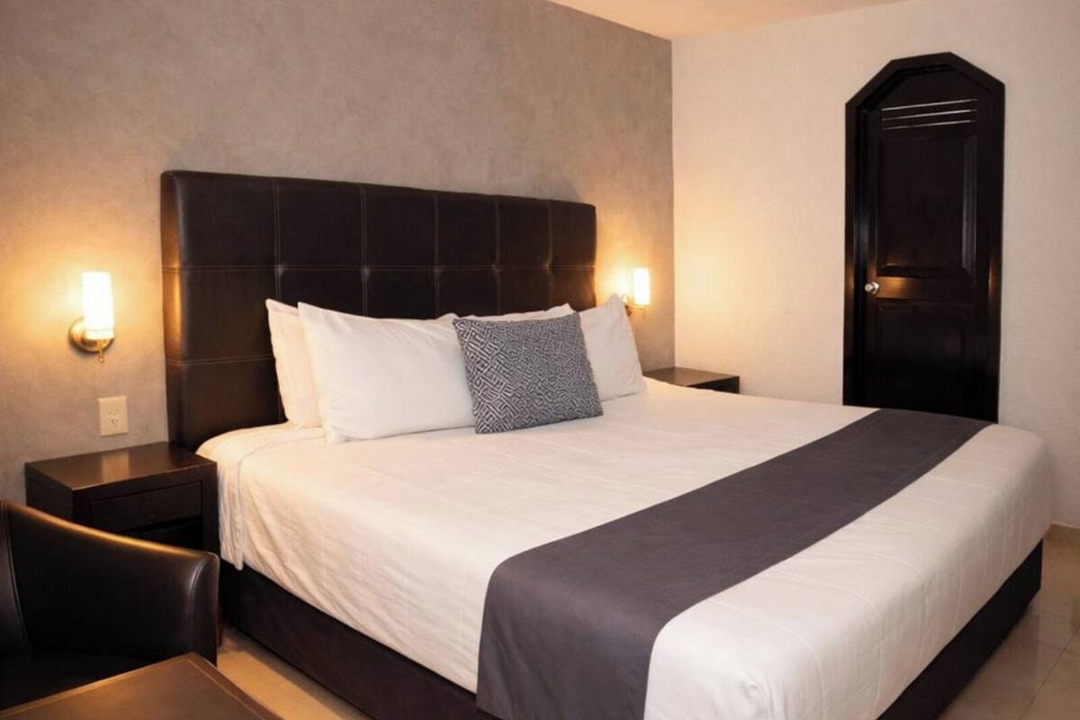A hotel room with a large bed, two bedside tables, a dark headboard, and a door.