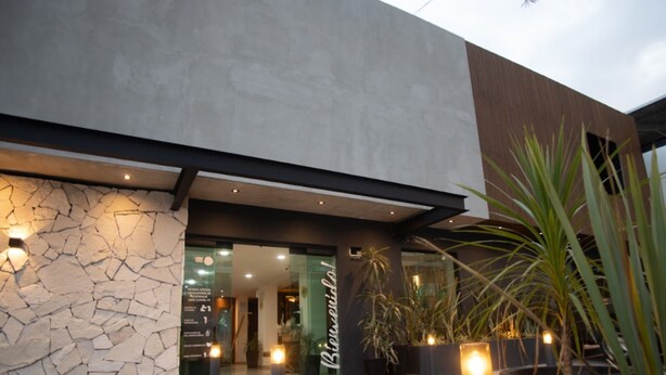 A modern building entrance with a stone facade, glass doors, and potted plants. - Hotel Ix by San Clemente Business Class (Tlaxcala)