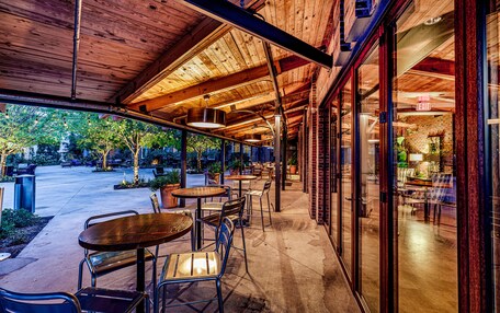 An outdoor patio area with tables and chairs, a brick wall, and a glass door leading to the interior.