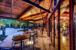 An outdoor patio area with tables and chairs, a brick wall, and a glass door leading to the interior.