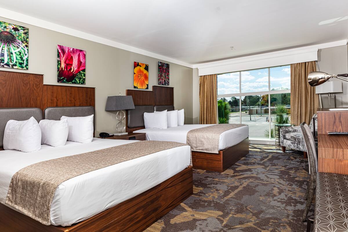 Habitación de hotel con dos camas, un escritorio, una lámpara y vistas al exterior.