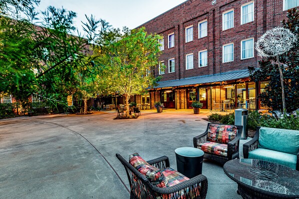 A courtyard with outdoor seating, a brick building, and trees.