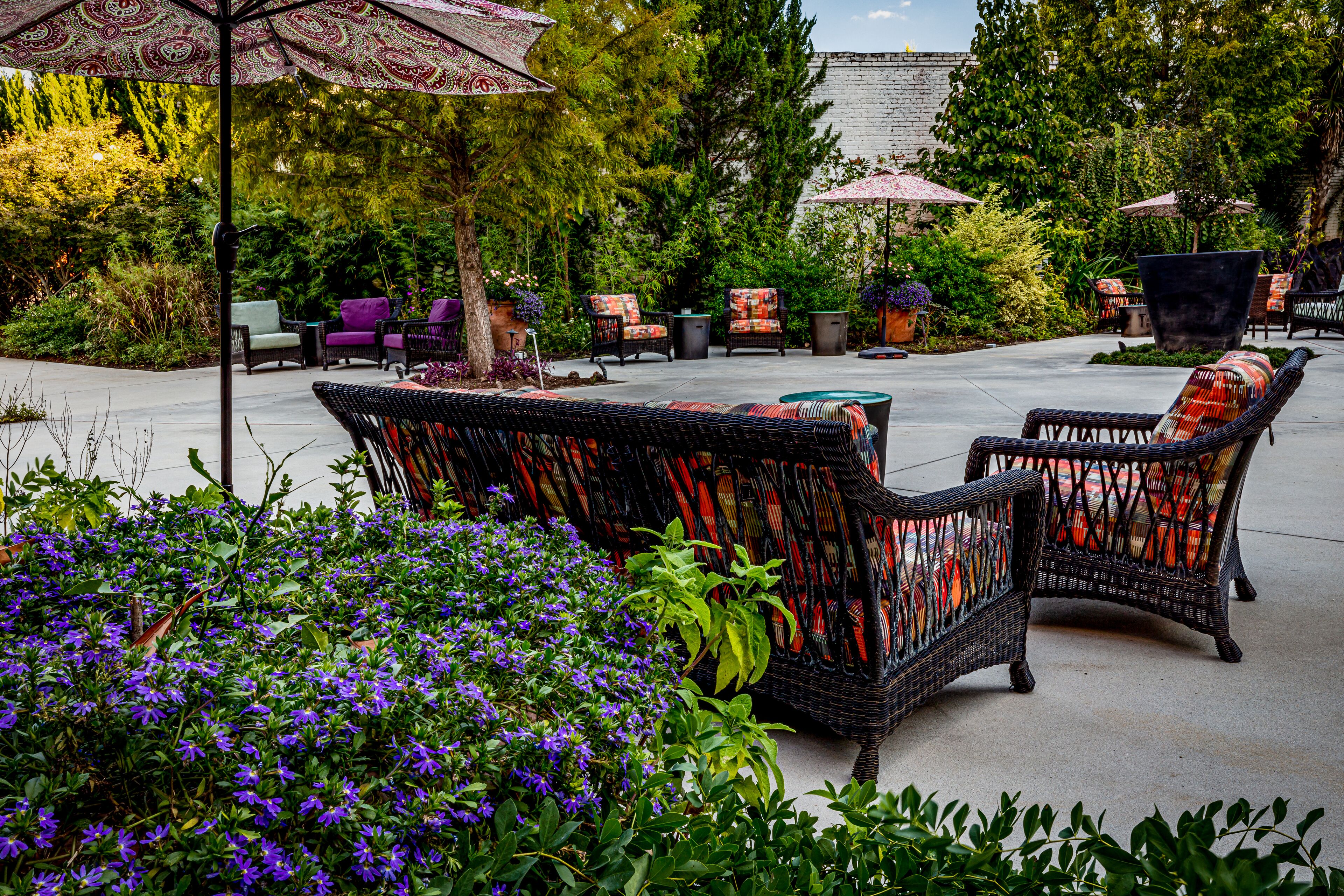 An outdoor patio area with wicker furniture, potted plants, and umbrellas.