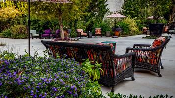 An outdoor patio area with wicker furniture, potted plants, and umbrellas.