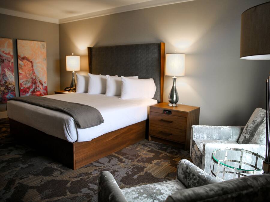A hotel room with a large bed, two bedside tables, a chair, and a lamp.