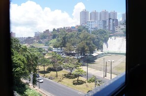 Un paisaje urbano con una combinación de edificios residenciales y rascacielos, una calle con vehículos, y una gran estructura blanca al fondo.