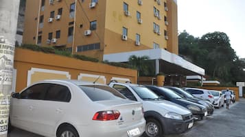 A row of parked cars in front of a yellow building with multiple air conditioning units.