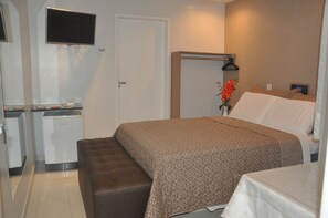 Una habitación de hotel con una cama, un escritorio pequeño con una computadora, un televisor y un banco.