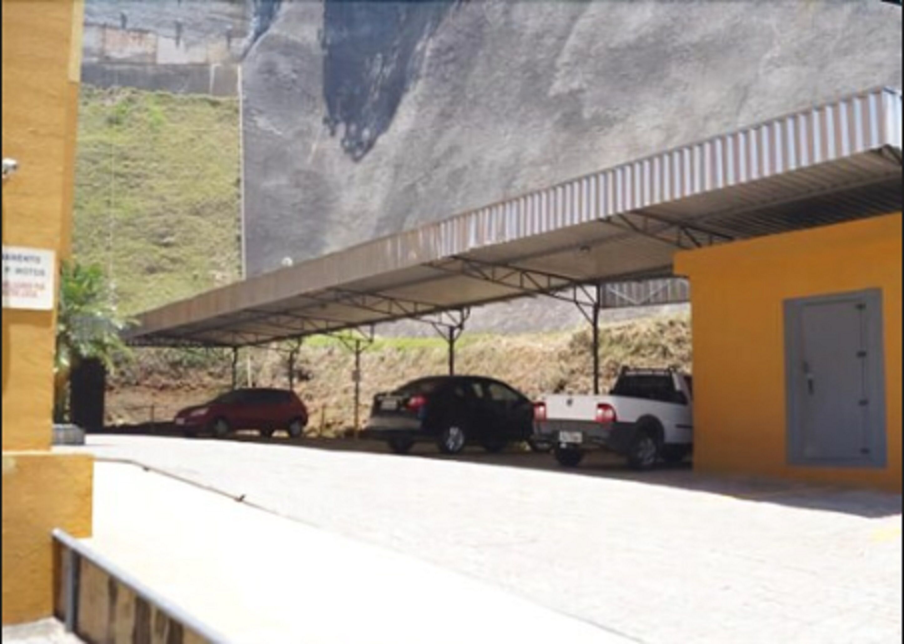 A parking area with a covered structure and a building with a door.
