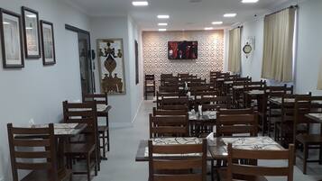Un grand espace dédié à la salle à manger, avec plusieurs tables et chaises en bois, un téléviseur à écran plat fixé au mur et un motif décoratif sur le mur.