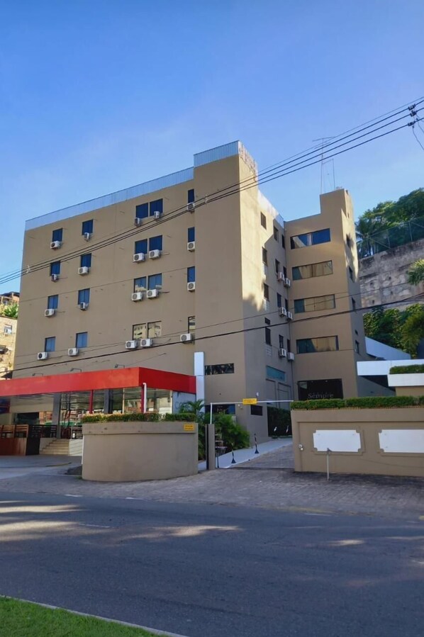 Un hotel de varios pisos con fachada plana, unidades de aire acondicionado y un toldo rojo sobre la entrada.