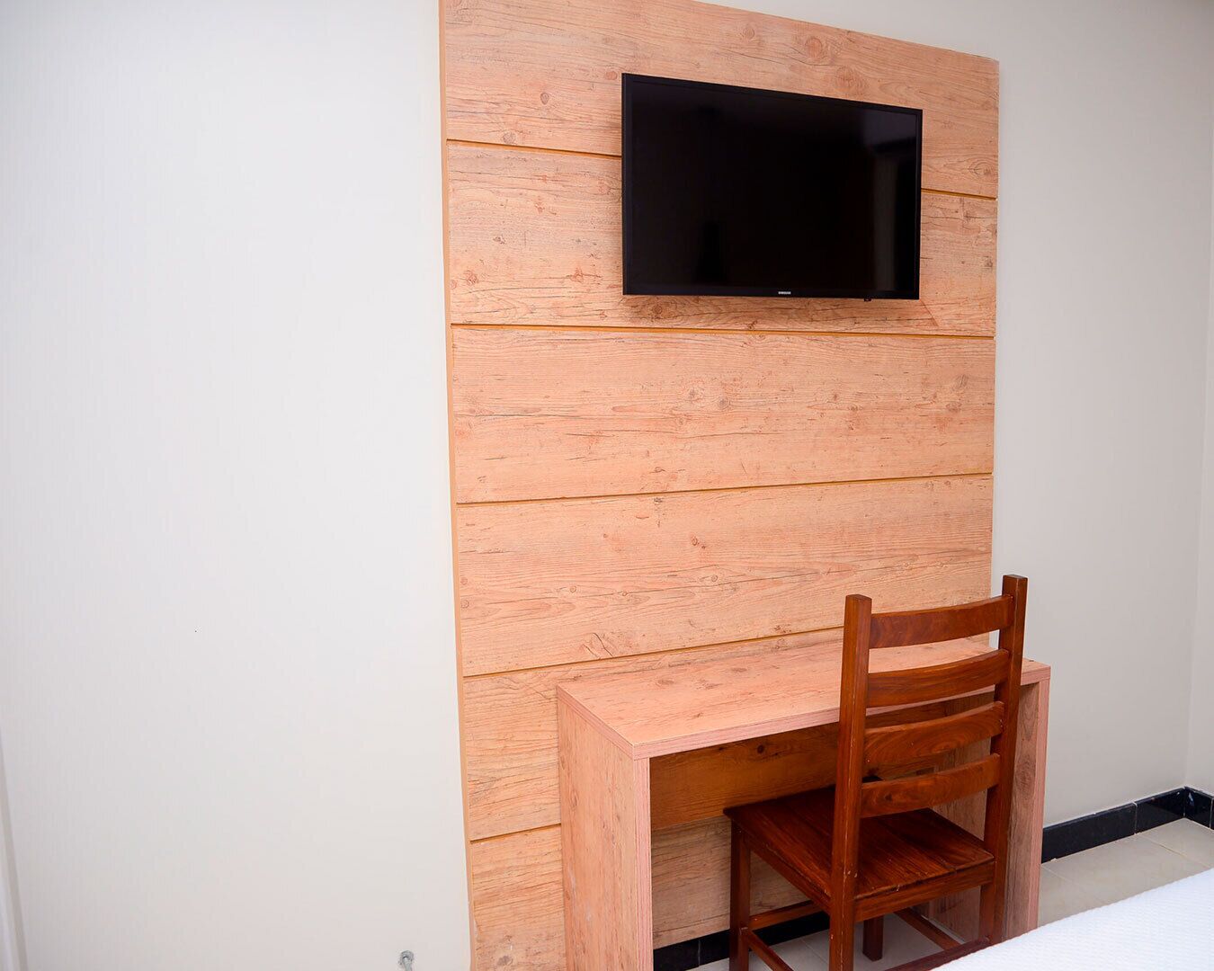A wooden wall with a flat-screen TV mounted above a wooden desk and chair.