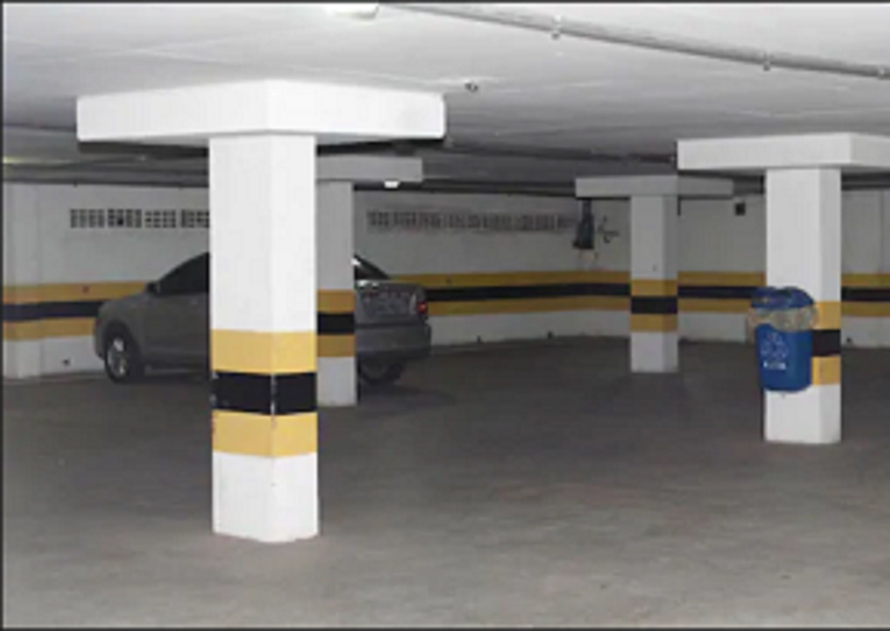 A parking garage with white pillars, yellow and black stripes, and a blue trash bin.