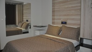 A modern hotel room with a large bed, a bedside table, a mirror, and a wall-mounted control panel.