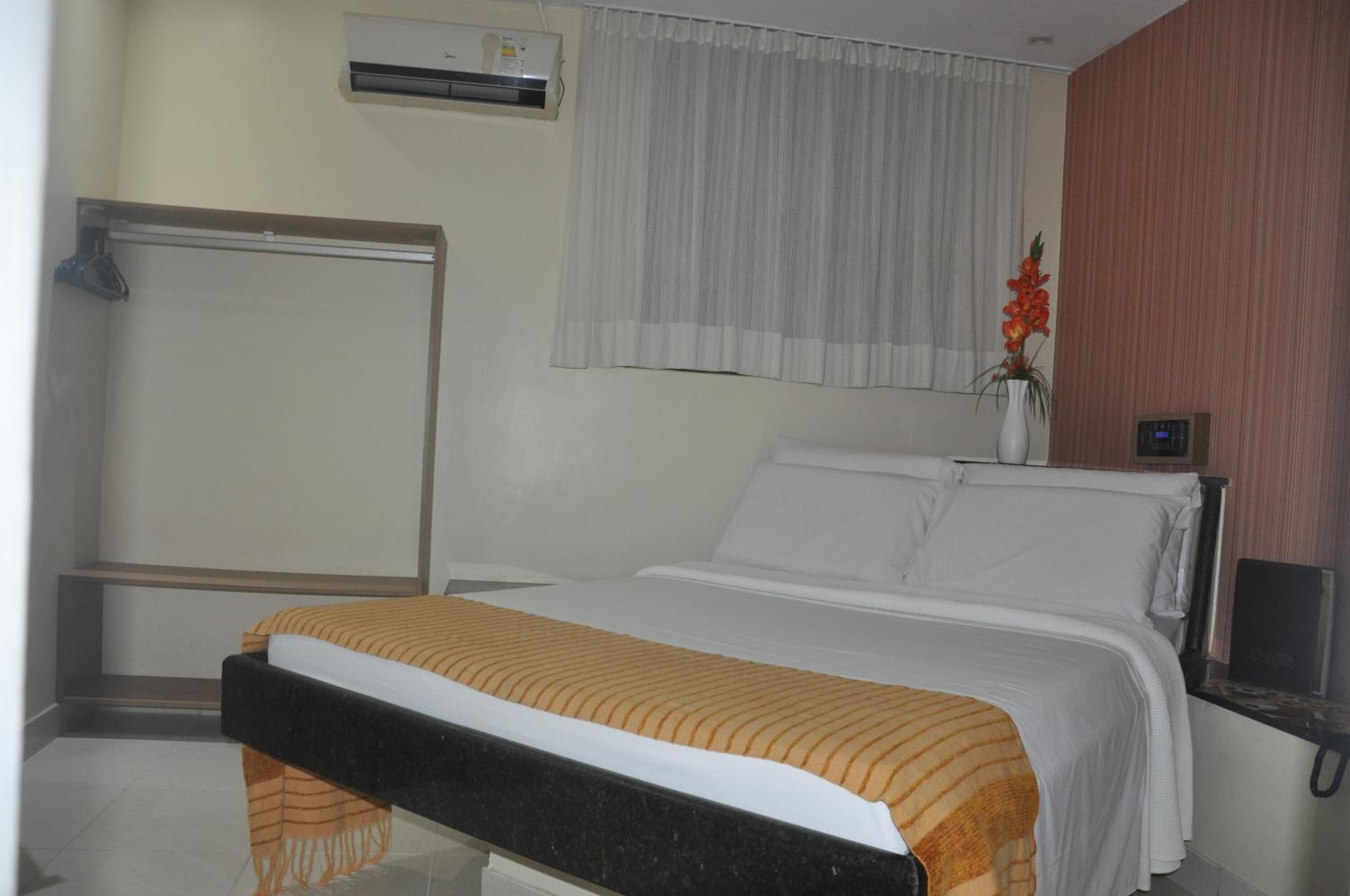Une chambre d’hôtel comprenant un lit, une table de chevet avec une lampe, une fenêtre avec des rideaux, un appareil de climatisation et un téléviseur fixé au mur.