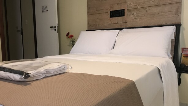 Ein ordentlich bezogenes Bett mit weißen Leinen, einer beige farbenen Strukturdecke und einem gefalteten Handtuch.