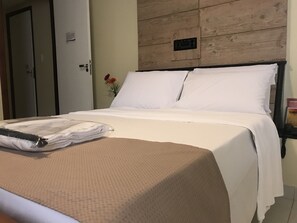 Una cama bien hecha con sábanas blancas, un edredón beige con textura y una toalla doblada sobre la cama.