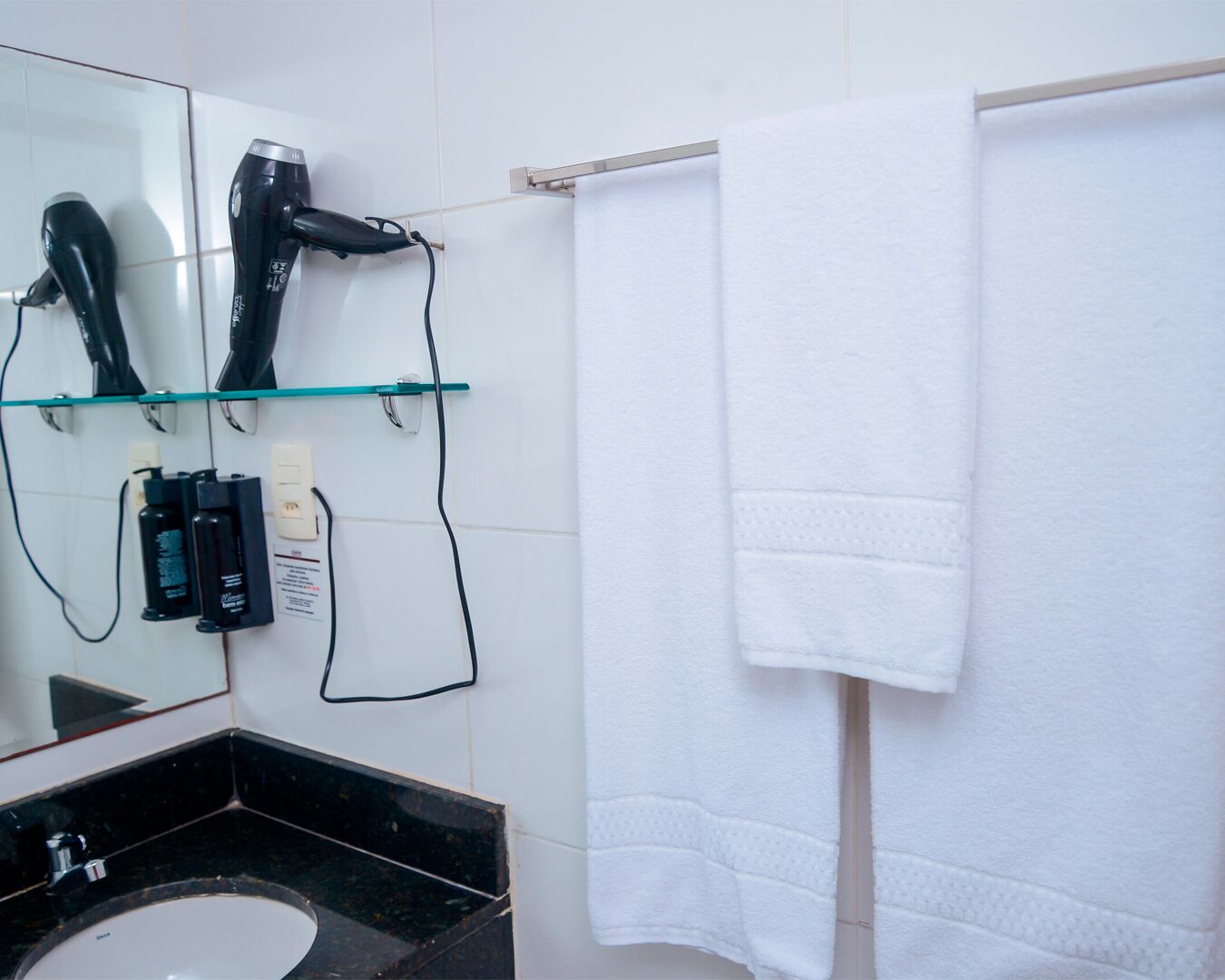 Casa de banho com lavatório preto, espelho, secador de cabelo e toalheiro com duas toalhas.