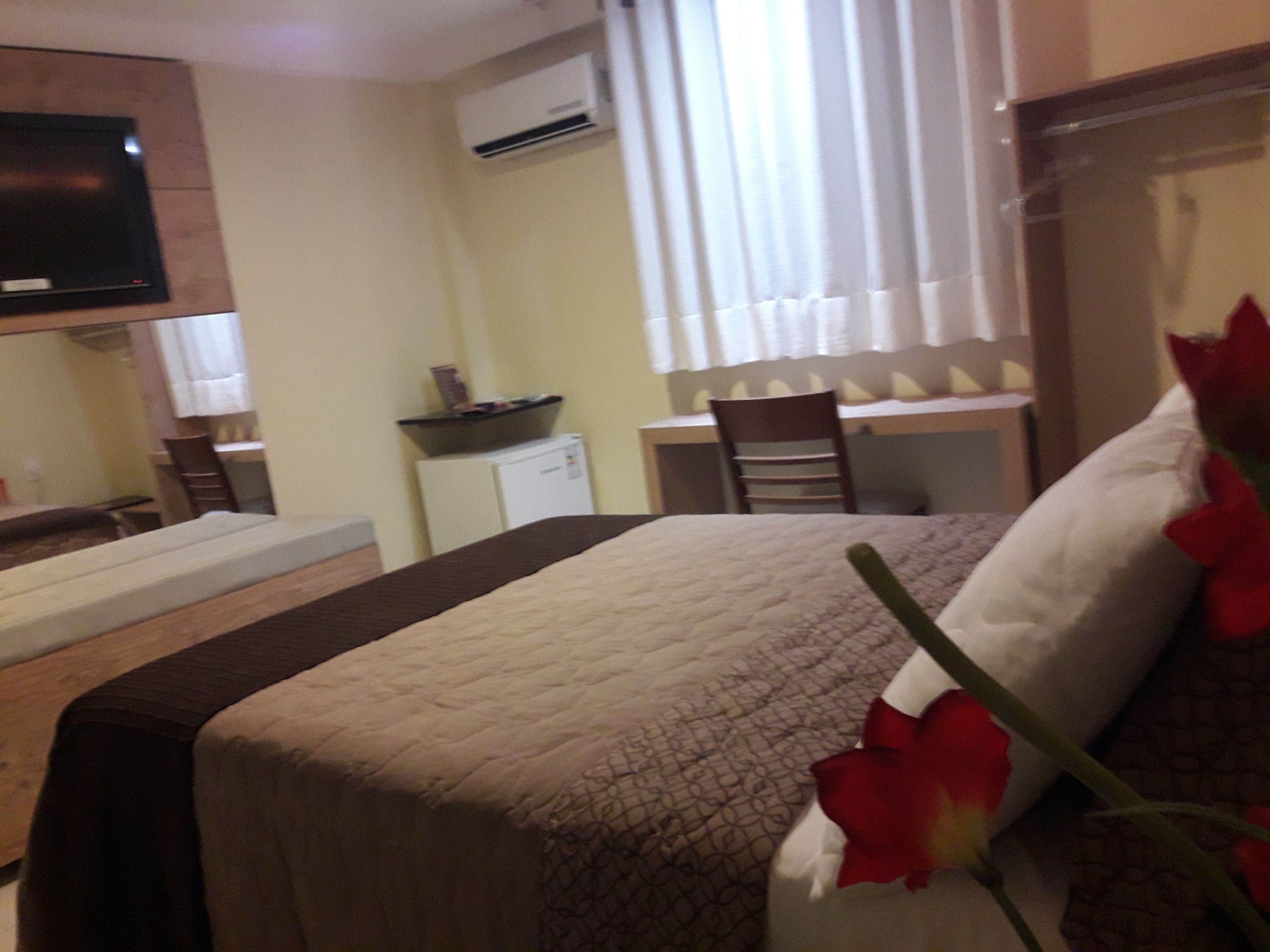 Une chambre d’hôtel équipée d’un lit, d’un bureau, d’une chaise, d’un climatiseur et d’un téléviseur fixé au mur.