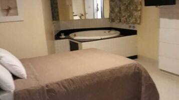 Un dormitorio con cama, un ventanal grande, un baño con bañera y un televisor de pantalla plana montado en la pared.