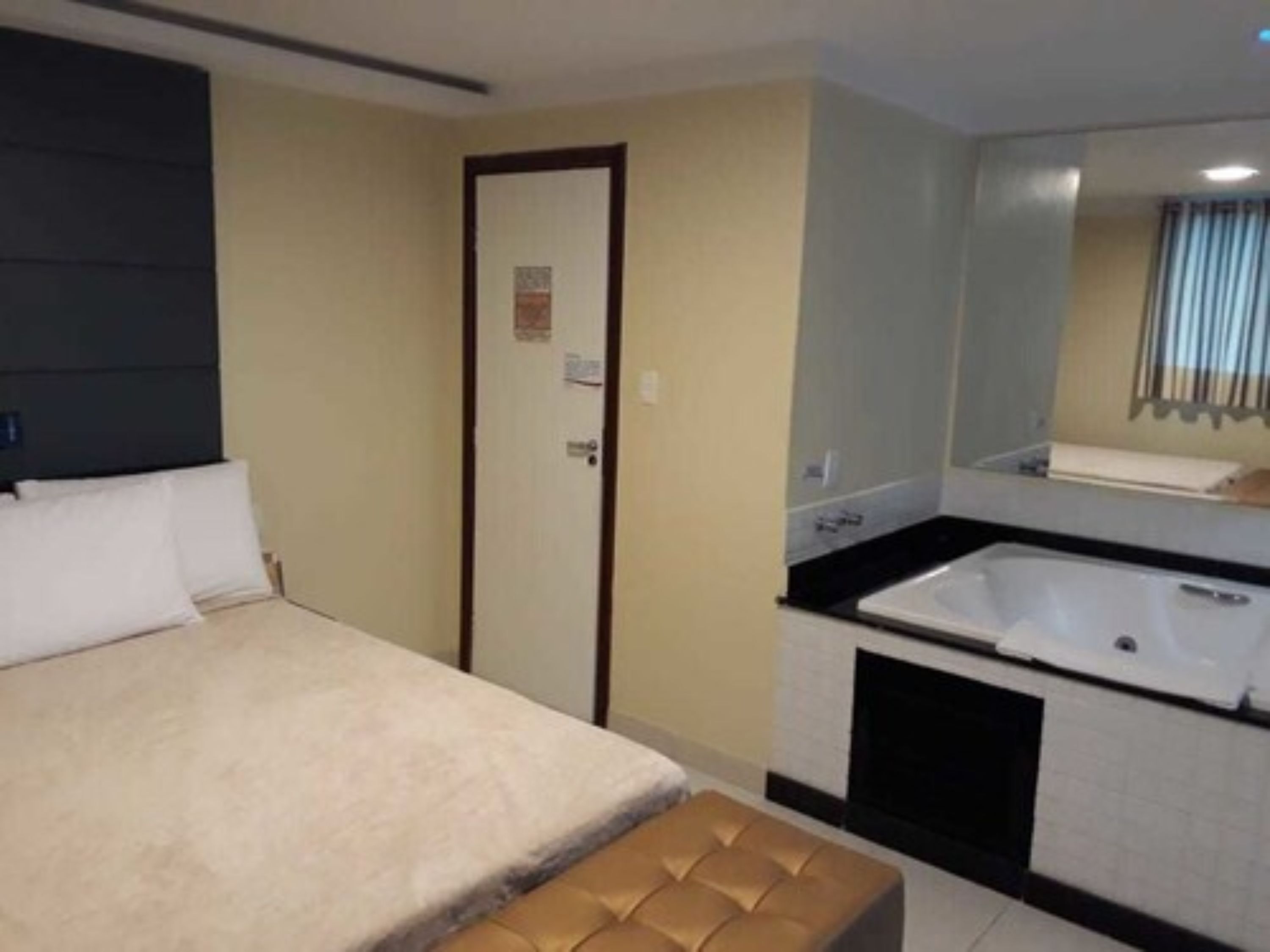 A hotel room with a bed, a bench, a bathroom with a bathtub, and a mirror.