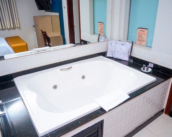 Un baño con una bañera blanca grande, una encimera negra y un espejo que refleja la habitación.