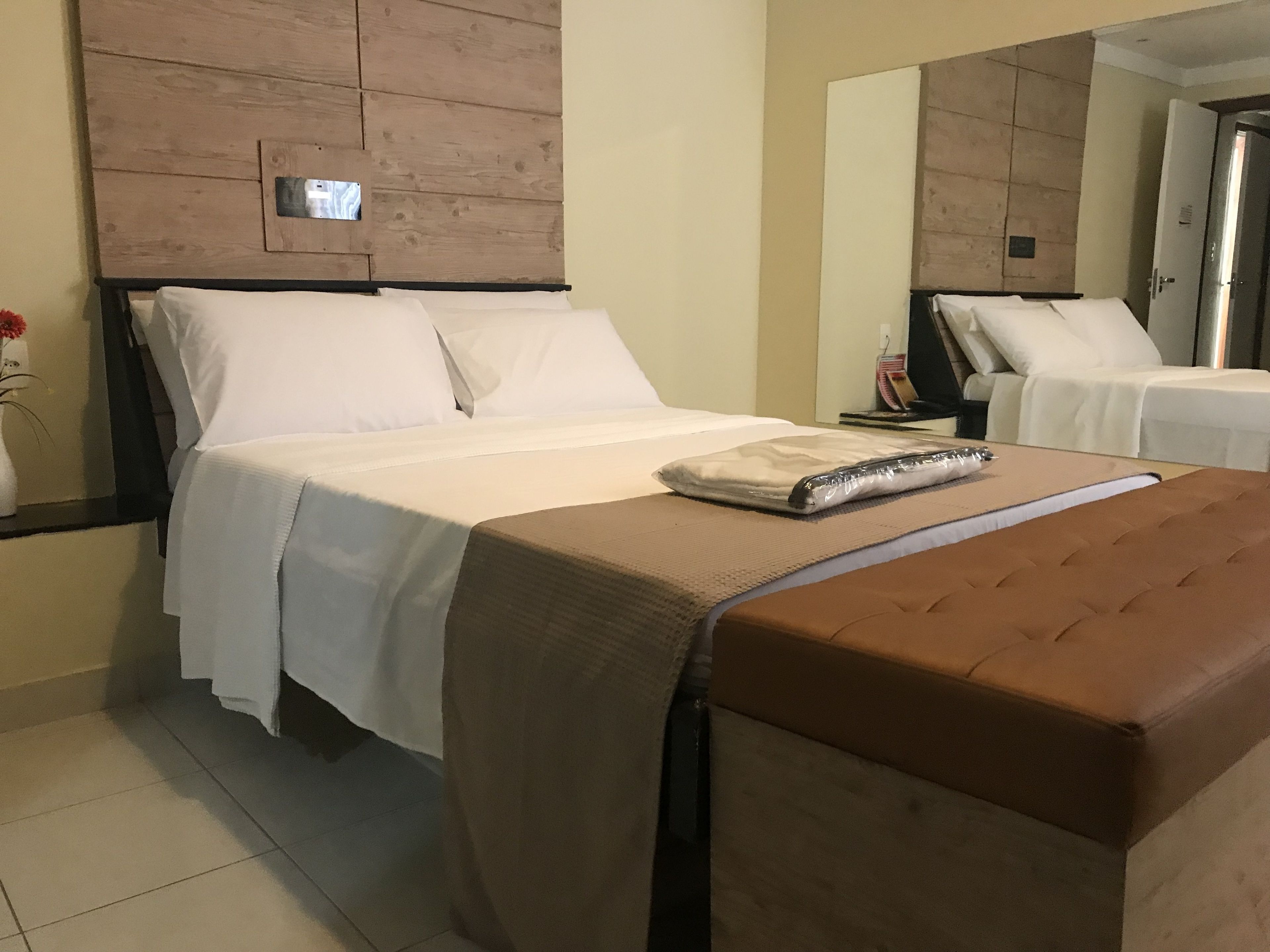 Una camera d'albergo con un letto, un comodino, uno specchio e una porta.