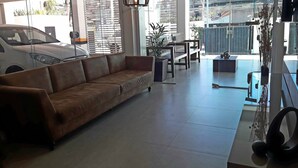 Ein modernes Wohnzimmer mit braunem Ledersofa, einem Esstisch mit Stühlen, einer kleinen Küchenzeile und einem großen Fenster mit Jalousien.