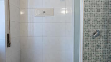 Une salle de bain comprenant des toilettes, une douche avec un mur carrelé et un porte-rouleau de papier toilette.