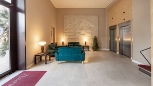 A modern lobby with a teal sofa, a large abstract wall art, two standing lamps, and a Christmas tree.
