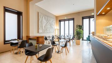 Un comedor moderno con mesas y sillas, una recepción y un amplio ventanal que proporciona luz natural.