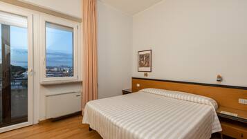 Une chambre à coucher comprenant un lit, une table de chevet, une fenêtre avec des rideaux, un radiateur et une lampe fixée au mur.