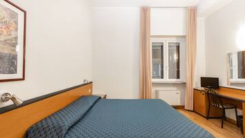 A bedroom with a bed, a desk, a chair, a television, and a window with curtains.