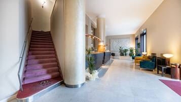 A modern hotel lobby with a marble staircase, a reception desk, seating area, and large columns.