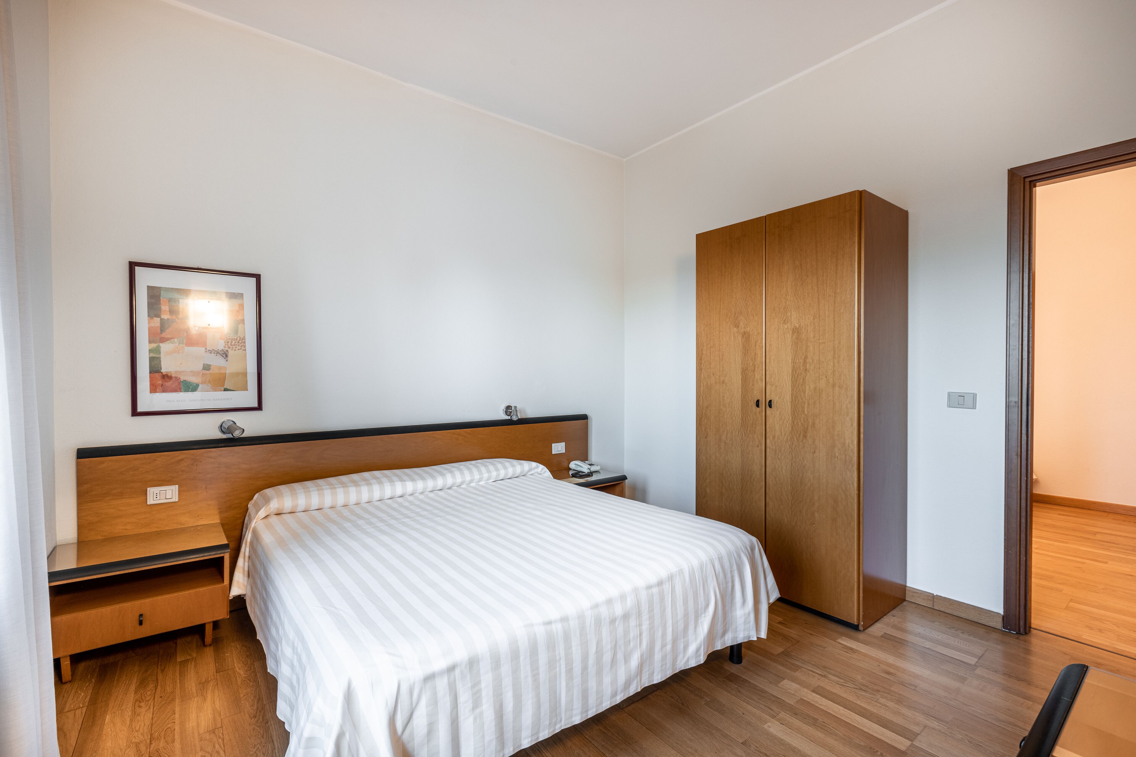 A bedroom with a bed, wooden wardrobe, nightstand, and a framed picture on the wall.