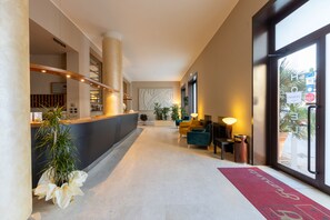 A hotel lobby with a reception desk, seating area, and large windows. - Hotel Nuova Grosseto (Grosseto)