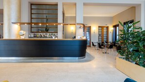 A modern hotel lobby with a curved reception desk, seating area, and a large plant.