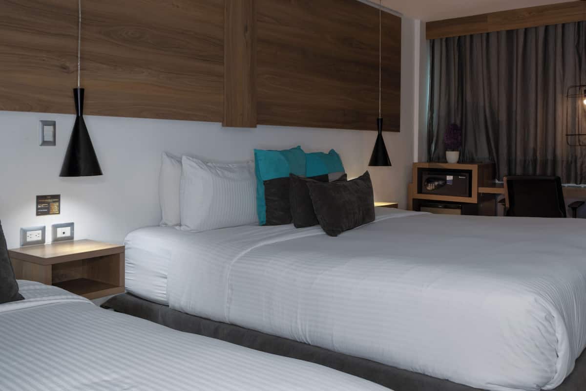 A hotel room with two beds, wooden headboards, a desk with a chair, and pendant lighting.