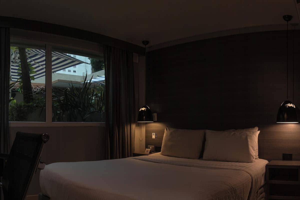 A dimly lit hotel room with a bed, a desk, and a window with curtains.