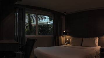 A dimly lit hotel room with a bed, a desk, and a window with curtains.