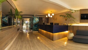 A modern hotel reception area with a wooden reception desk, a seating area, and a wall-mounted TV. - The Blue Hotel. (Cartagena)