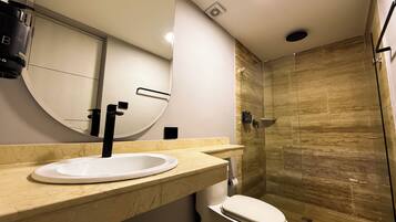 Un baño moderno con un espejo redondo, un lavabo blanco y una ducha con cerramiento de vidrio.