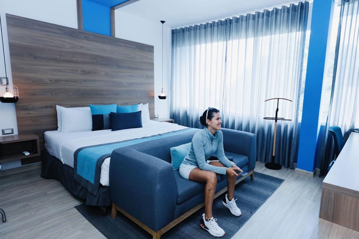 A modern hotel room with a bed, sofa, and a large window with curtains.