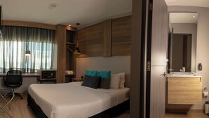 A modern hotel room with a large bed, a desk with a chair, a wardrobe, and a bathroom with a mirror and sink. - The Blue Hotel. (Cartagena)