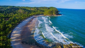 A coastal landscape with a curved beach, dense greenery, and a clear view of the ocean. - Pousada Bambu (Itacaré)